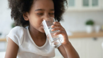 Little girl drinks clean still mineral water from glass at home